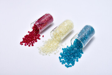 transparent red, blue and natural masterbatch granules spilling from a glass tube, isolated on a...