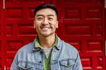 close up portrait of young adult of asian ethnicity looking at camera smiling on colorful red background - obrazy, fototapety, plakaty