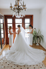 Wedding morning. Bridesmaids help put on the white wedding dress. A young woman is preparing to meet her groom and having fun with her friends