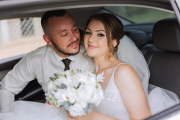 The bride looks out of the car window. Close-up portrait of a pretty shy bride in a car window. The groom kisses the bride