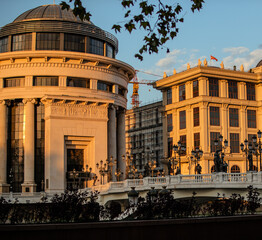 two old-style buildings in a city at sunset, with traffic lights: Skopje, North Macedonia