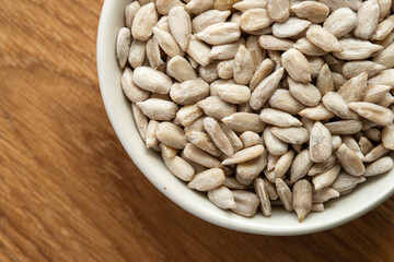 Bowl of peeled raw sunflower seeds on a wooden background. Top view.