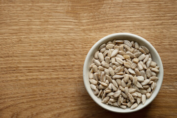 Bowl of peeled raw sunflower seeds on a wooden background. Copy space. Top view.