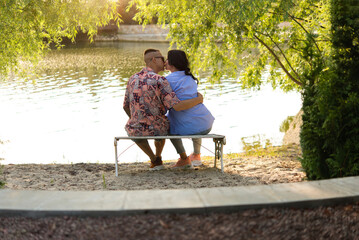 Happy couple in love kisses and cuddles on a bench on the lake. Sunset over the water.