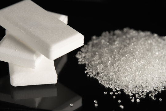 A stack of dextrose glucose tablets and a pile of white granulated sugar on black glass.