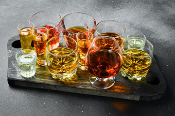A set of glasses with different alcoholic beverages: rum, tequila, whiskey or brandy, cognac and vodka, on a stone table. Strong aged alcoholic drinks. On a stone background.