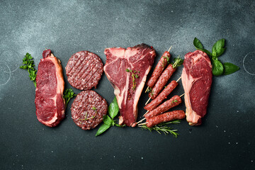 A set of juicy raw steaks, kebabs, cutlets and meat with spices and herbs. On a black stone...