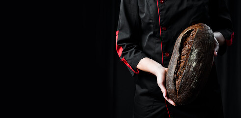 Fragrant black oval bread in female hands. Homemade rye bread. - obrazy, fototapety, plakaty