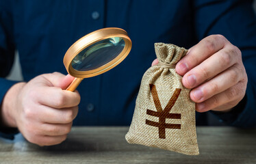 A man examines a chinese yuan or japanese yen money bag through a magnifying glass. Investigating...