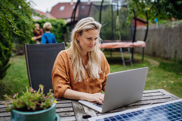 Businesswoman, freelancer or manager working outdoors in garden, garden homeoffice. Remote work from backyard. Laptop is charging with solar charger. Concept of working remotely.