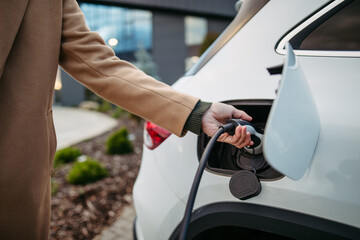 Close up of businessman charging electric car before going to office. An electric vehicle charging...