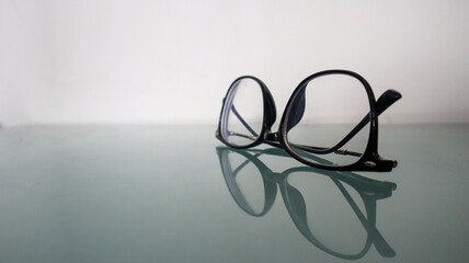 Glasses with black frames are placed upside down on a blue glass table surface which reflects the...