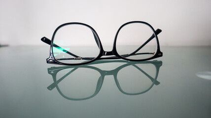 Glasses with black frames are placed upside down on a blue glass table surface which reflects the...