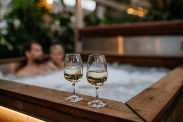 Two wine glasses on hot tub, couple relaxing, enjoying romantic wellness weekend in spa. Concept of...