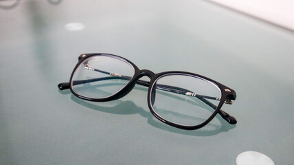 Glasses with black frames are placed upside down on a blue glass table surface which reflects the...