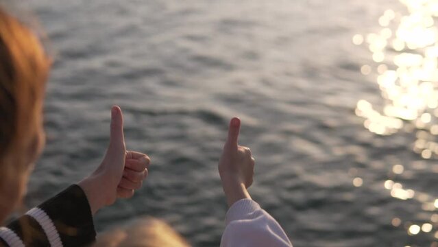 Mom and daughter show a clas gesture with their hand against the background of the sunset in the sea