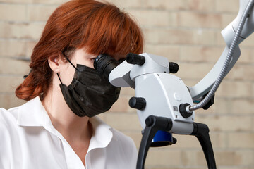 Close-up of female dentist using binocular microscope for dental treatment. Modern high-precision...