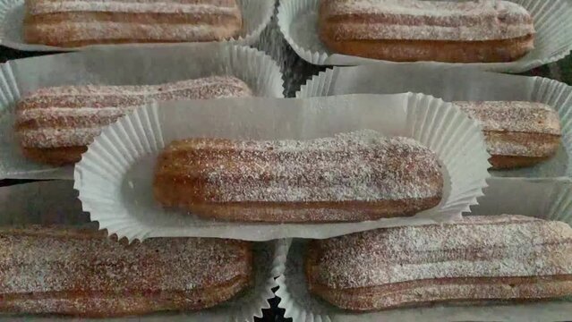 Freshly baked eclairs sprinkled with white powdered sugar. Coffee with eclair for breakfast or dessert is a great addition to the drink. Many eclairs lie beautifully on the table. slow motion concept