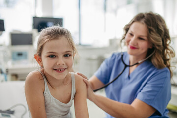 Orthopedist examines the spine, posture, and spinal deformities of little girl. Girl visiting paediatrician for annual preventive exam. Concept of preventive health care for children. - obrazy, fototapety, plakaty