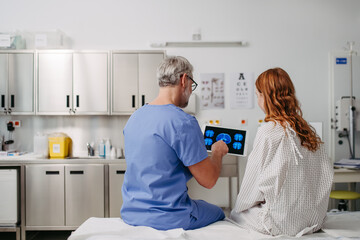 Rear view of doctor showing teenage patient MRI scan on tablet, discussing test result in emergency...