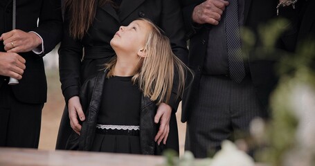 Mourning, grief and family with girl at funeral, flowers on coffin, death and sad child at service in graveyard. Support, loss and people at casket in cemetery with kid crying at grave for burial.