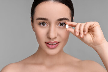 Beautiful young woman with vitamin pill on grey background