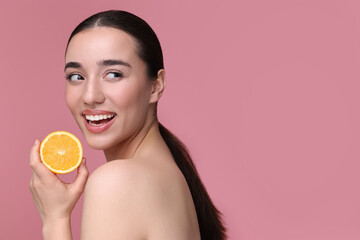 Beautiful young woman with piece of orange on pink background. Space for text