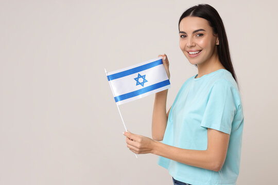 Happy young woman with flag of Israel on beige background, space for text