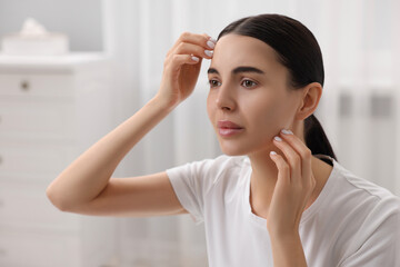 Woman with dry skin checking her face indoors