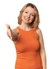 Blonde middle-aged Caucasian woman in studio stretching hand at camera in greeting gesture.