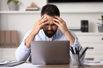Man suffering from headache at workplace in office