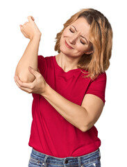 Blonde middle-aged Caucasian woman in studio massaging elbow, suffering after a bad movement.