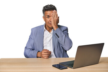 Elegant businessman at desk with laptop having fun covering half of face with palm.