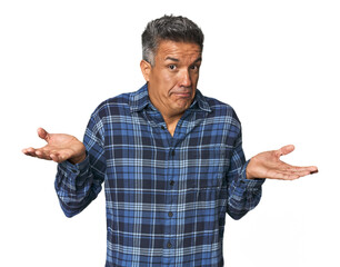 Middle-aged Latino man doubting and shrugging shoulders in questioning gesture.