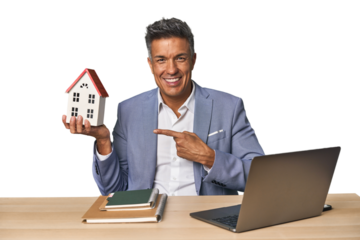 Joyful middle-aged Hispanic realtor with laptop and mini house