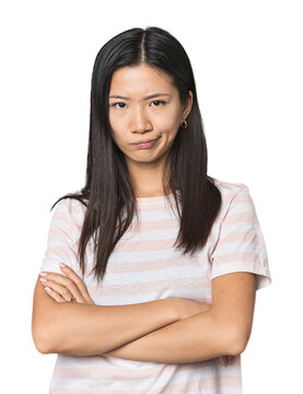 Young Chinese woman in studio setting frowning face in displeasure, keeps arms folded.