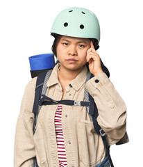 Chinese woman geared up for mountain activities pointing temple with finger, thinking, focused on a task.