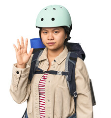 Chinese woman geared up for mountain activities smiling cheerful showing number five with fingers.