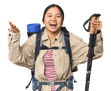 Young Chinese woman with hiking gear ready for adventure receiving a pleasant surprise, excited and raising hands.