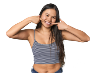 Young Chinese woman in gray top, studio smiles, pointing fingers at mouth.