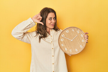 Woman holding clock on yellow backdrop feels proud and self confident, example to follow.