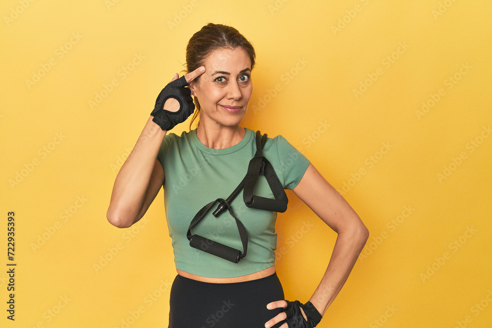 Wall mural Woman with resistance bands on yellow set showing a disappointment gesture with forefinger.