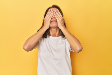 Middle-aged caucasian woman on yellow afraid covering eyes with hands.