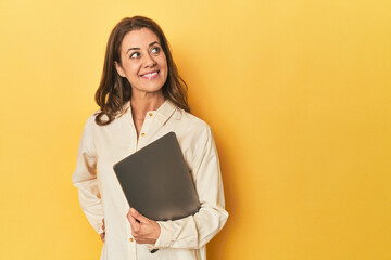 Middle-aged woman using laptop in yellow studio