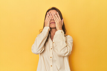 Middle-aged caucasian woman on yellow afraid covering eyes with hands.