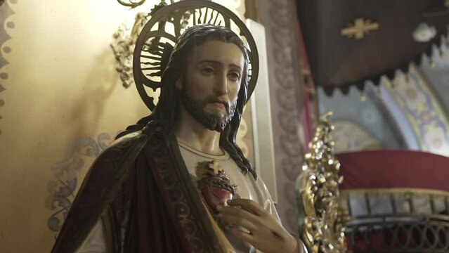 Statue of Jesus with a sacred heart, halo, and robe inside a church, with ornamental details and soft lighting enhancing its spiritual ambiance.