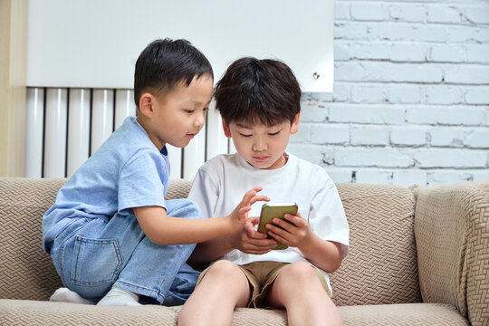 Two brothers sitting on the sofa playing with their phones