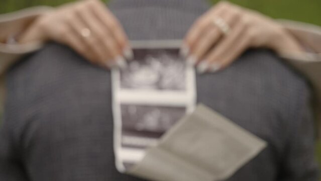 A woman holding an ultrasound scan behind a man's back, both wearing rings, depicting a couple expecting a child, perfect for stock video content related to pregnancy, family, and love.
