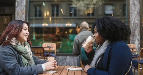 Young multiracial women having coffee break at vintage bar outdoor during winter time - Cozy beverage and lifestyle concept - Soft focus on asian girl face