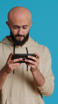 Vertical Video Joyful muslim man playing mobile video games in studio, enjoying online competition using smartphone app. Arabic gamer having fun with roleplaying challenge contest. Camera 1.